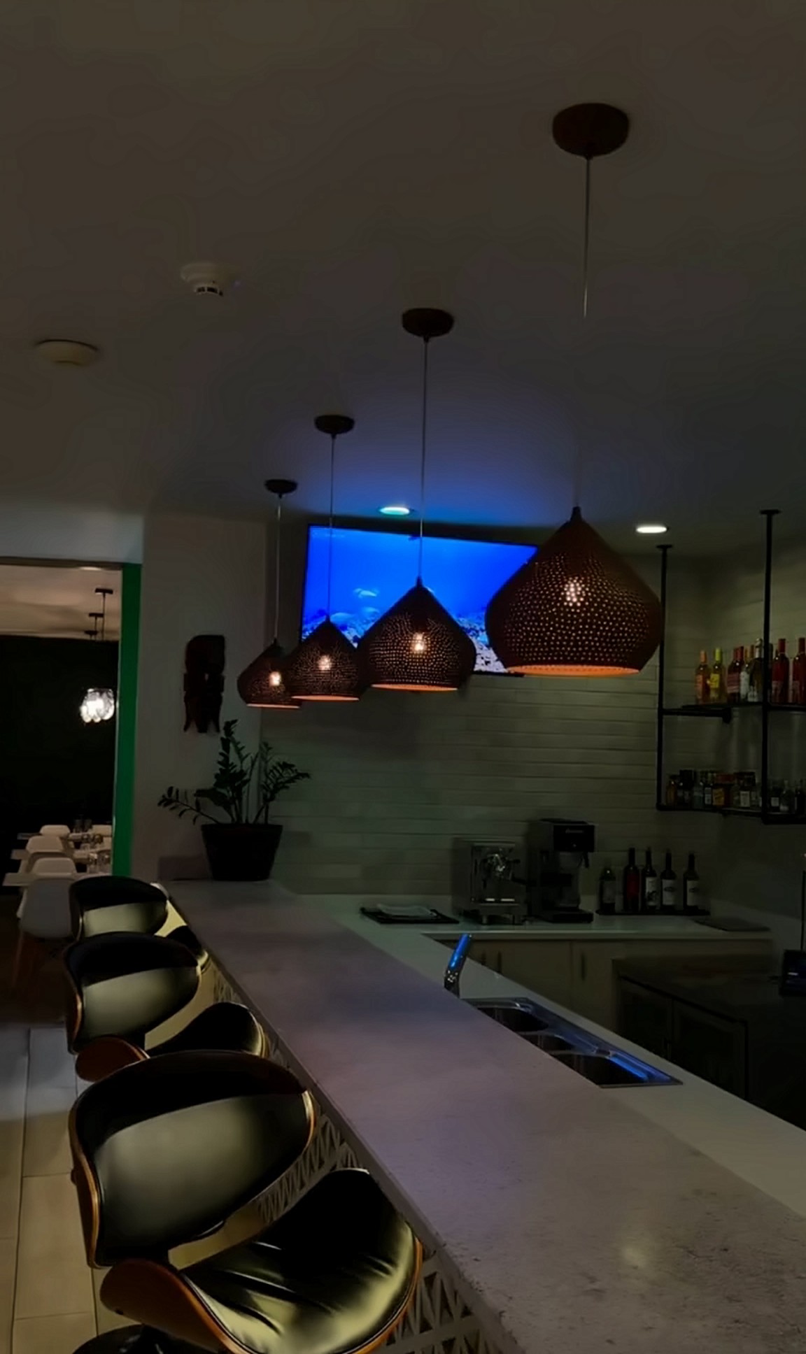 Leather bar stools along a stone bar top under a row of copper pendant lamps.