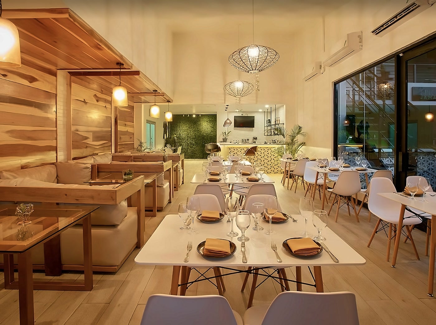 The dining room by day: pale oak booths, white tables set with tan napkins and woven pendant lamps.